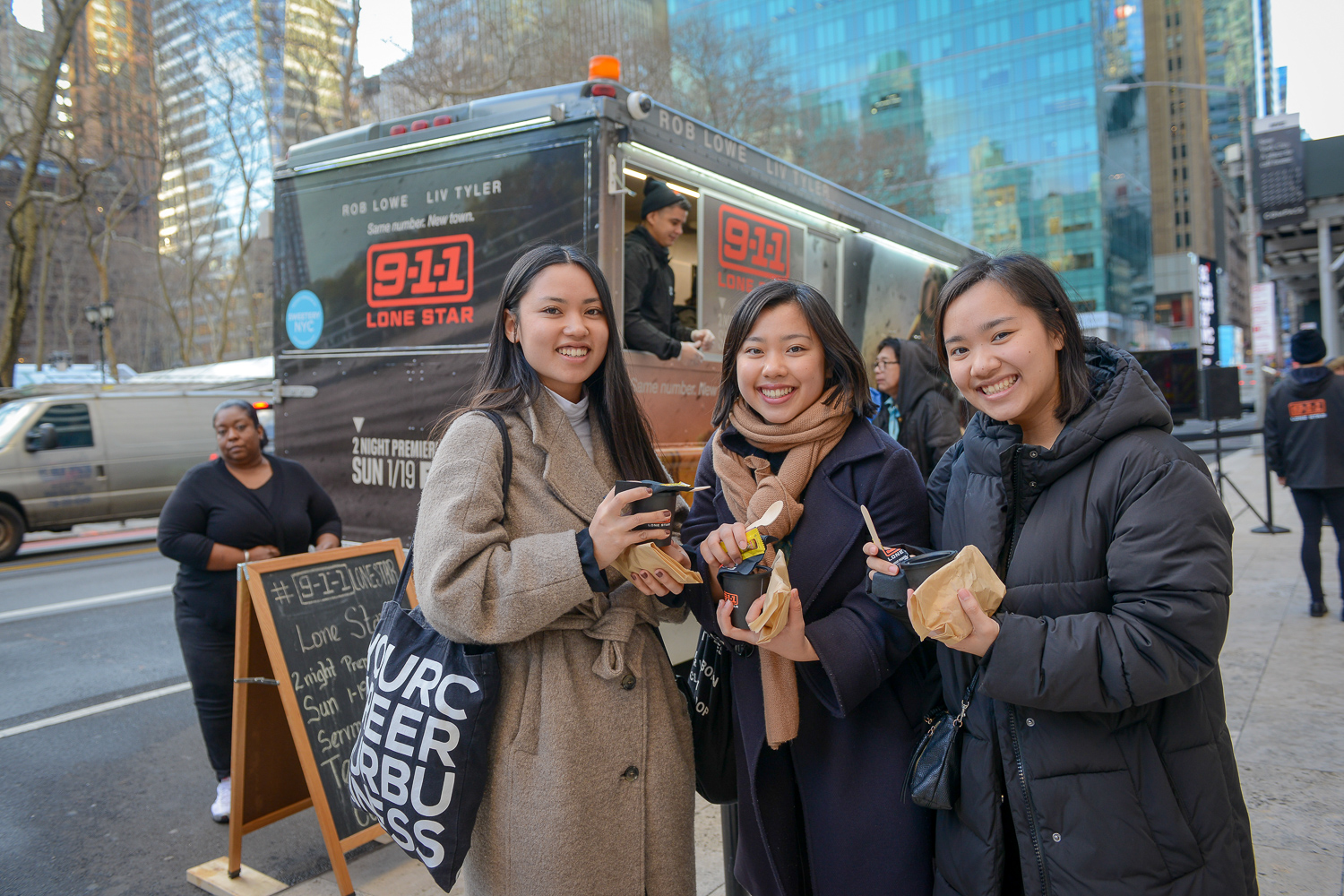 Three attendees holding branded cups and snacks near a 9-1-1 Lone Star activation truck.