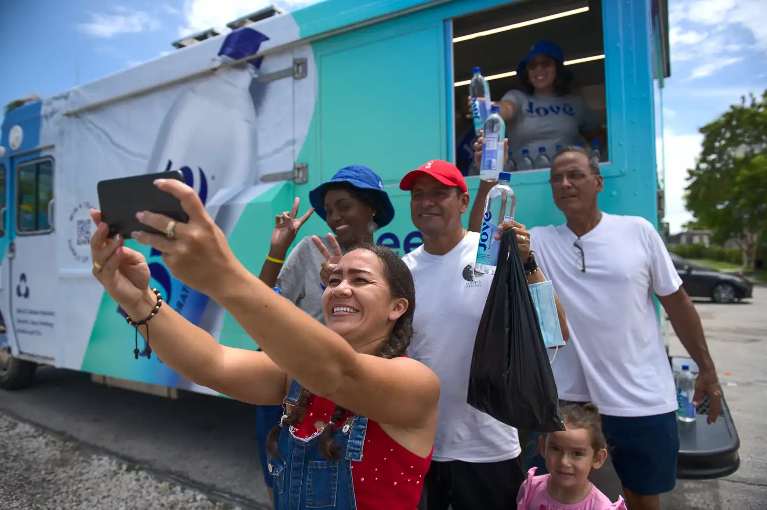 Visitors pose for a selfie while receiving bottled water from the jove promotional glass box truck.