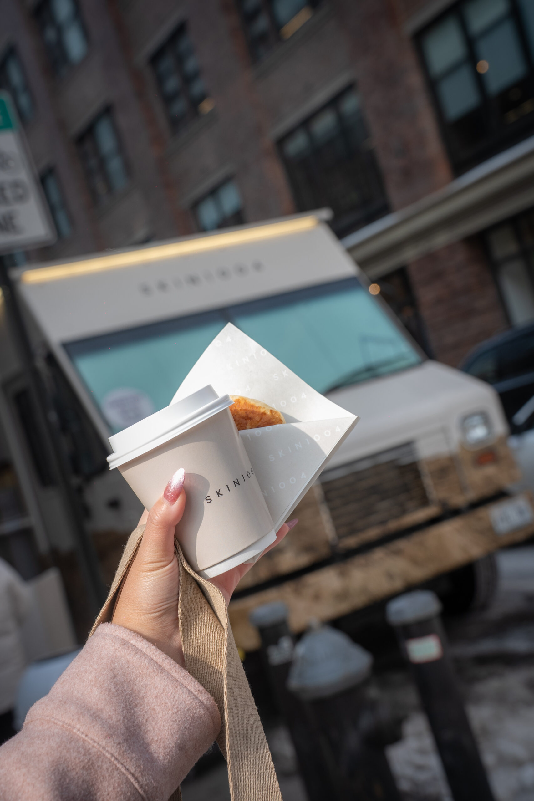 Hand holding a SKIN1004 sample cup and pastry with the branded truck behind it.