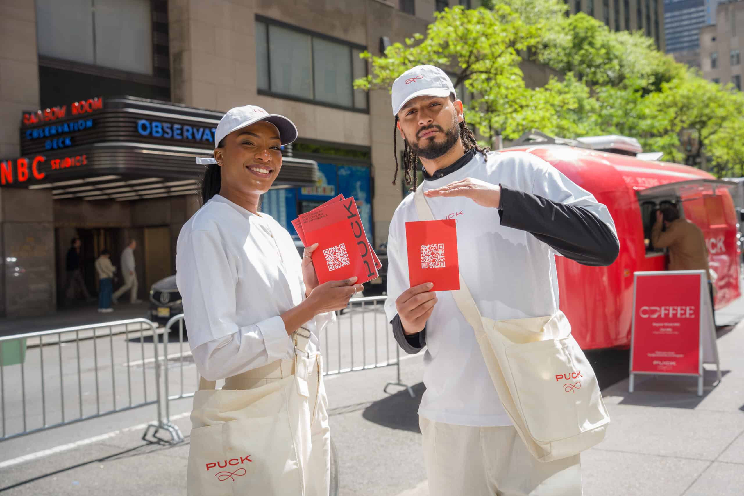 Two Puck brand ambassadors holding red promotional cards in front of the mobile activation.