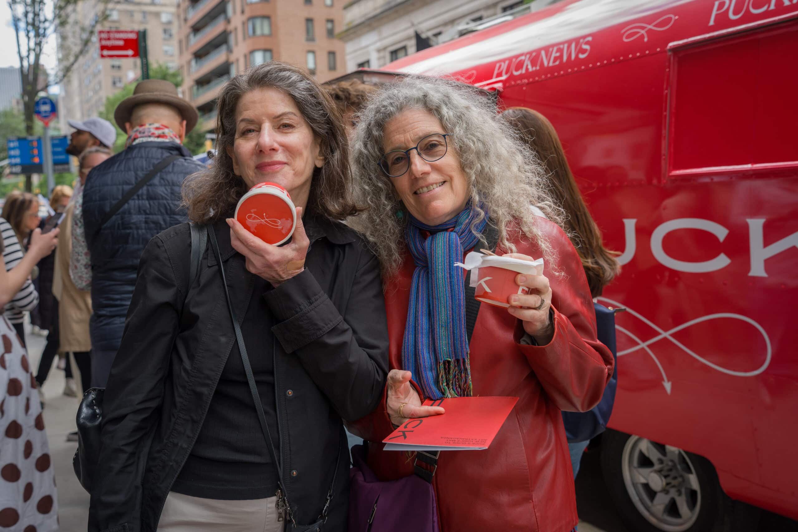 Two guests holding red sample cups beside the Puck trailer.