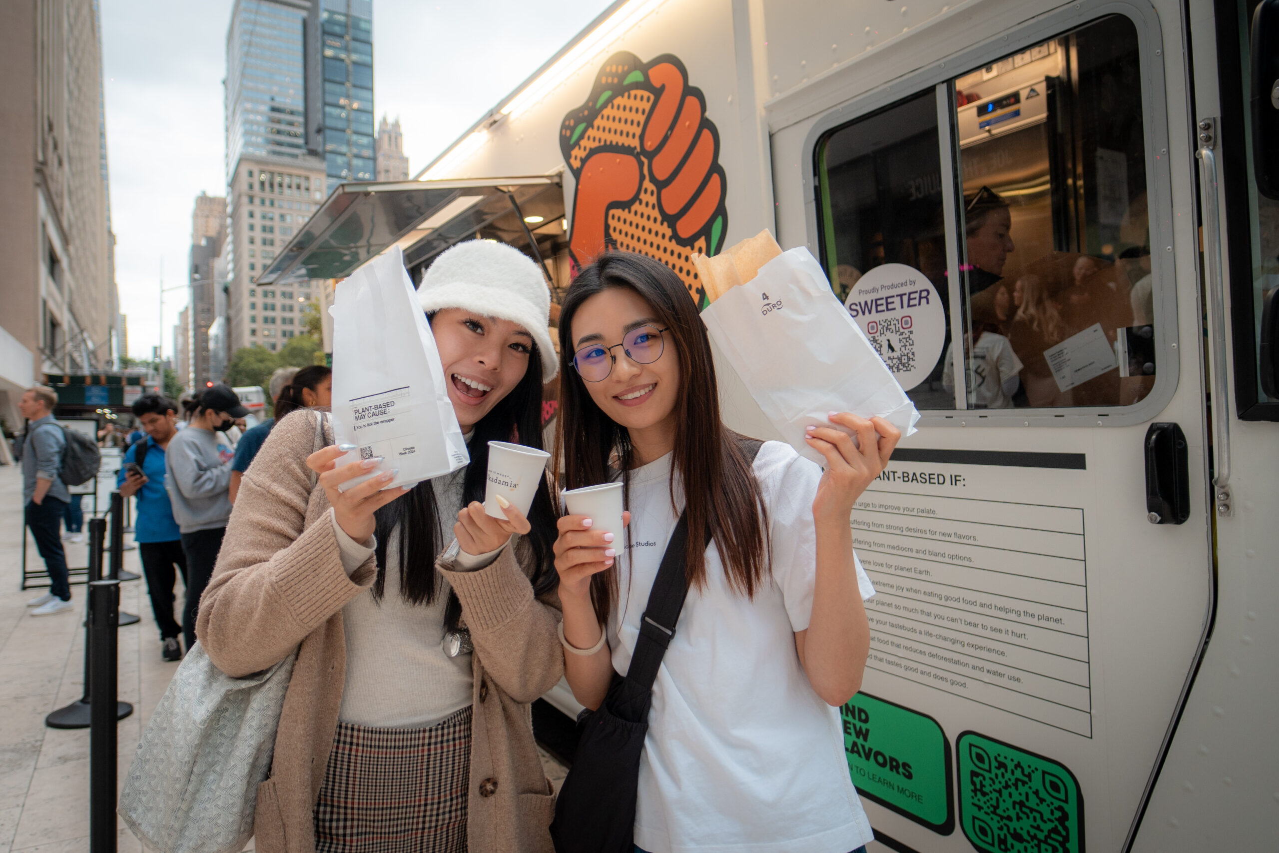 Two customers holding Grow Plant Based sample bags and drinks in front of the branded food truck activation.