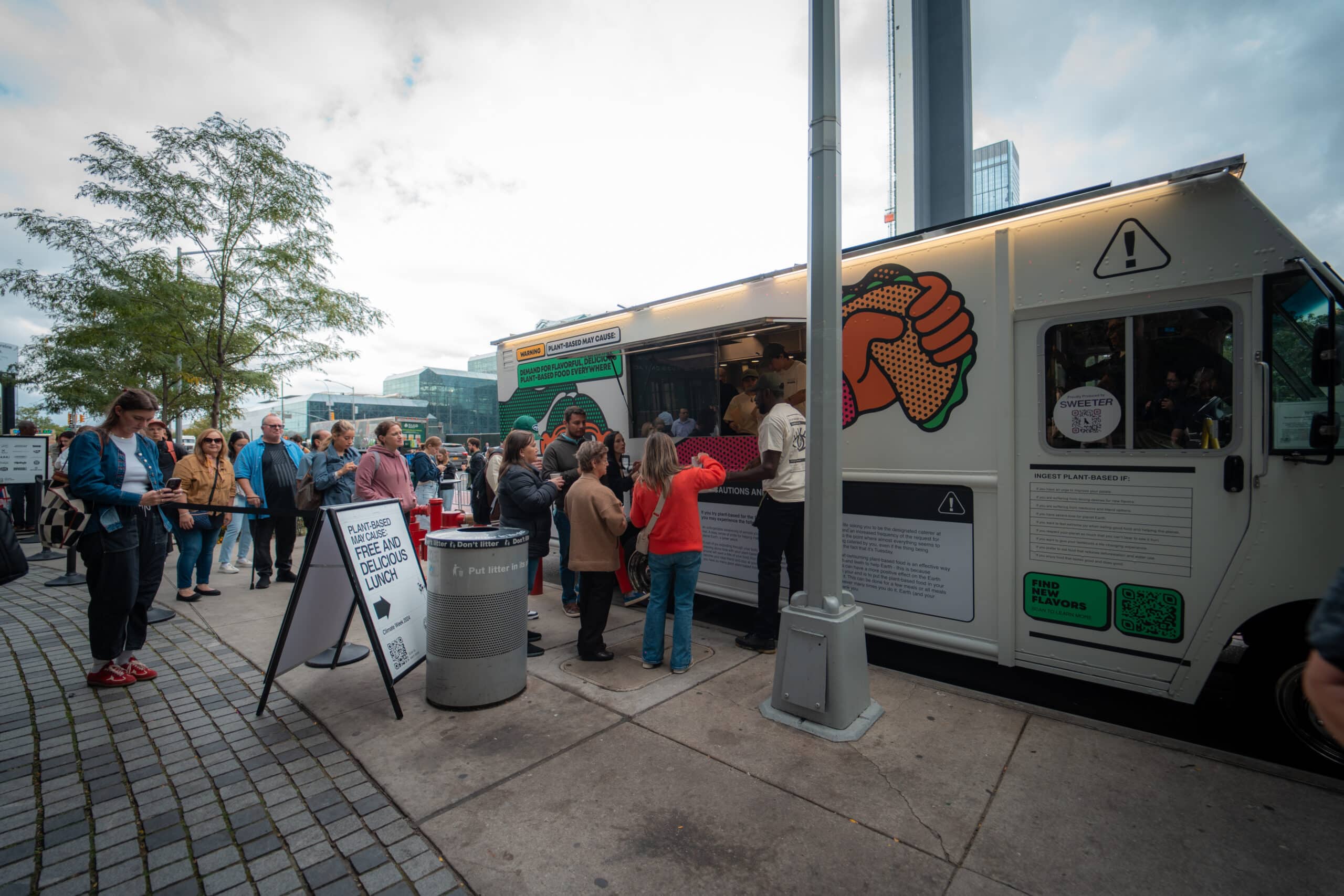 Customer line waiting at a Grow Plant Based branded food truck for free plant-based lunch samples in the city.