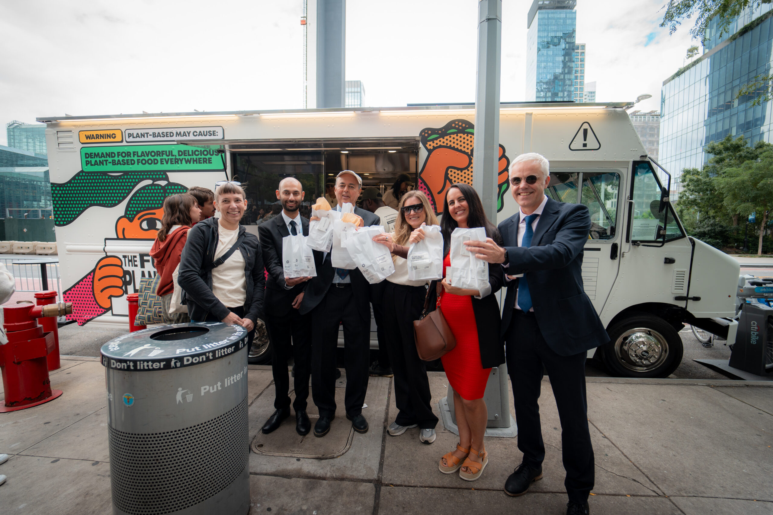 Guests posing with food samples in front of the Grow Plant Based branded food truck during a street activation.