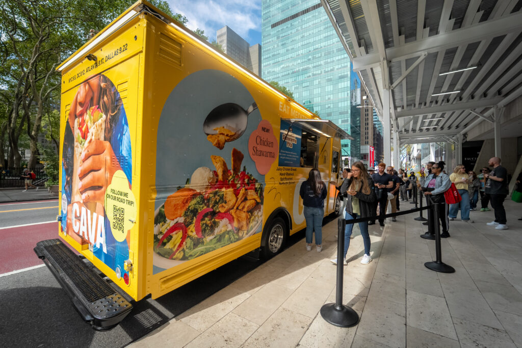 CAVA branded yellow food truck with customers lined up for chicken shawarma pita samples during a city activation.