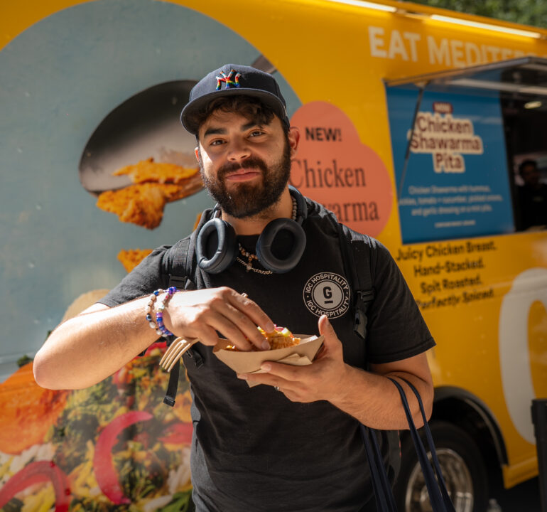 Customer eating a CAVA chicken shawarma sample in front of the yellow branded food truck promotion.