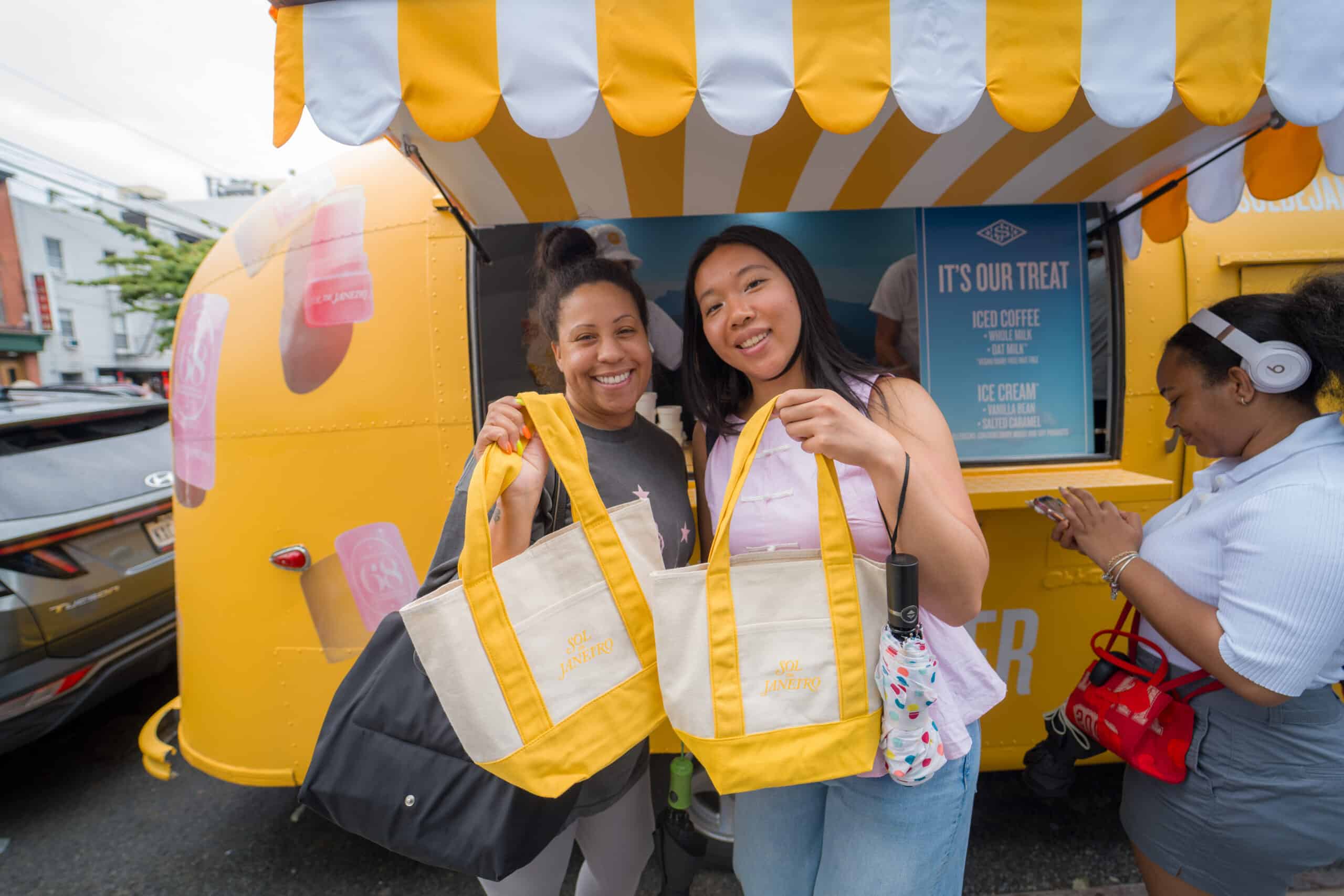 Two brand ambassadors posing with tote bags beside the yellow mobile activation.